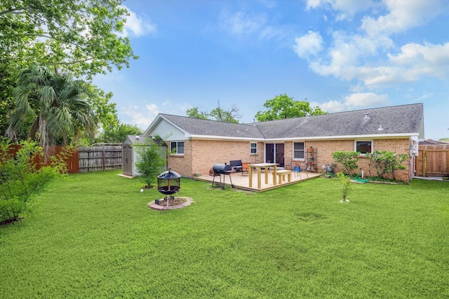 rear view of property featuring a storage unit, brick siding, a fenced backyard, a lawn, and a fire pit