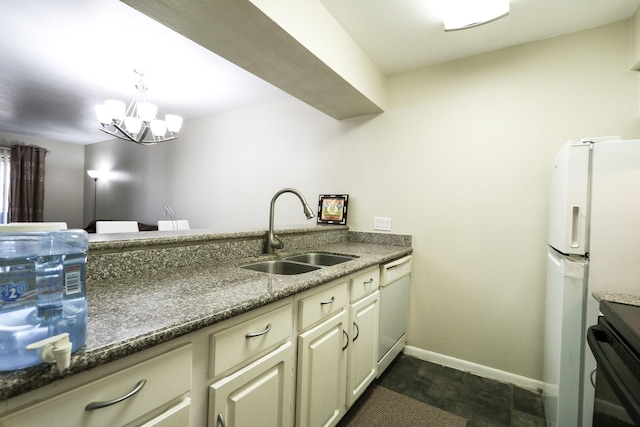 kitchen featuring a sink, baseboards, dark stone countertops, a chandelier, and white appliances