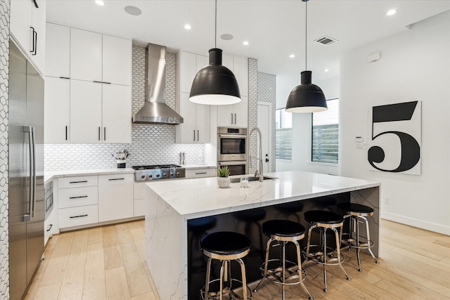 kitchen featuring wall chimney range hood, stainless steel appliances, visible vents, and light wood-style floors