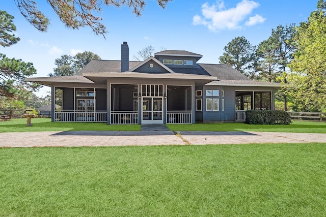 back of house with a chimney, roof with shingles, a lawn, a sunroom, and fence