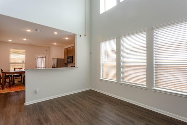 unfurnished living room with visible vents, dark wood finished floors, baseboards, and a healthy amount of sunlight