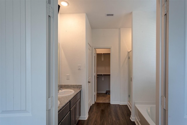 full bath with visible vents, wood finished floors, a washtub, a walk in closet, and a sink
