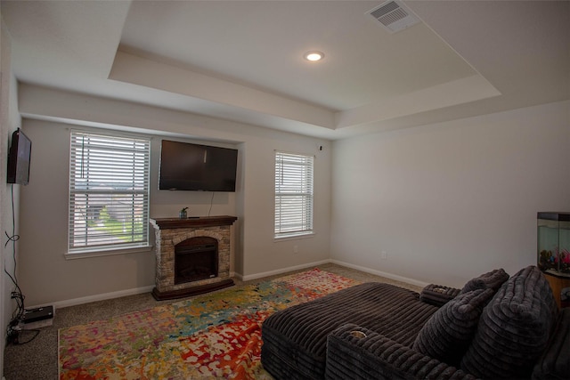 living room with carpet floors, visible vents, baseboards, a stone fireplace, and a tray ceiling