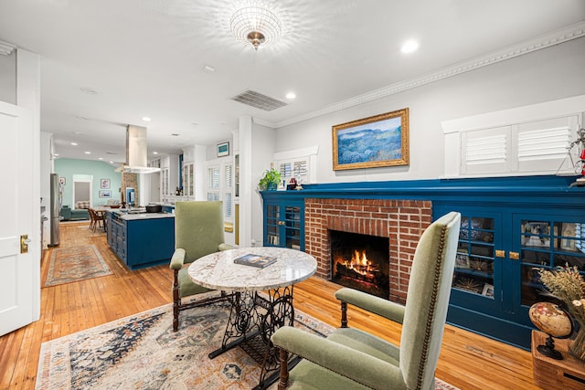 living area with visible vents, a brick fireplace, ornamental molding, recessed lighting, and light wood-style flooring