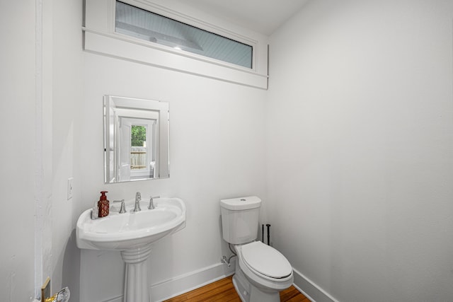 half bathroom featuring baseboards, a sink, wood finished floors, and toilet