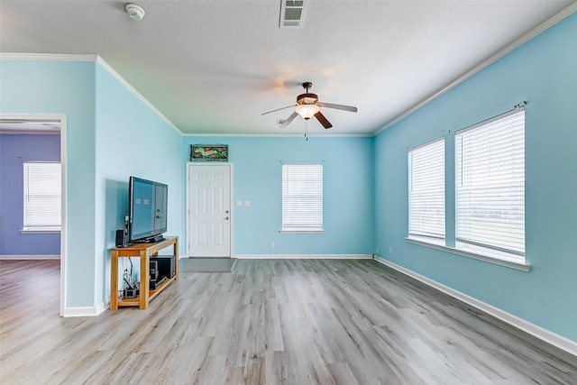 unfurnished living room featuring a ceiling fan, visible vents, wood finished floors, baseboards, and ornamental molding