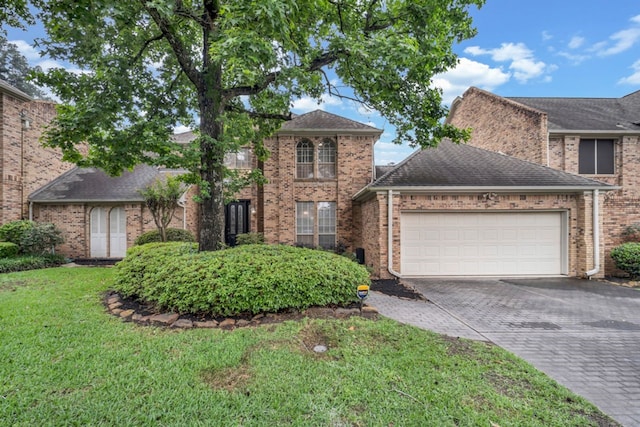traditional-style house with a front lawn, decorative driveway, brick siding, a shingled roof, and an attached garage