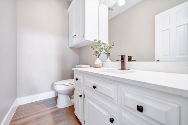 half bathroom featuring vanity, baseboards, wood finished floors, and toilet