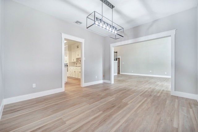 unfurnished dining area featuring an inviting chandelier, light wood-style floors, baseboards, and visible vents