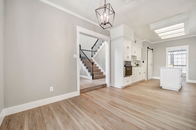 unfurnished living room with ornamental molding, stairs, light wood-style floors, a barn door, and a chandelier