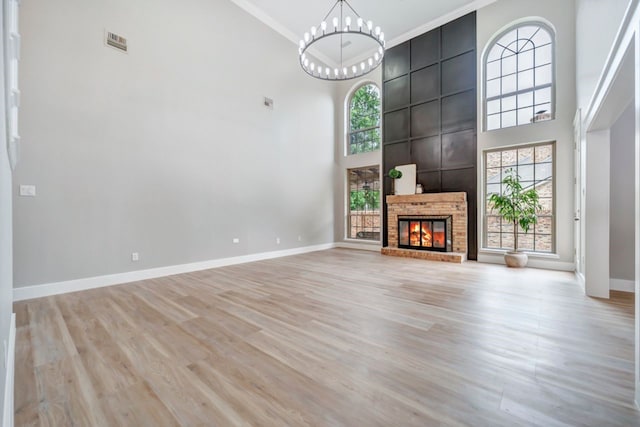 unfurnished living room with an inviting chandelier, light wood-style floors, a high ceiling, and visible vents