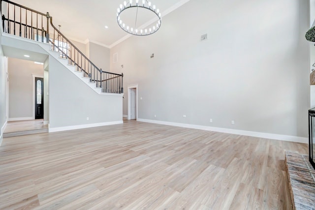 unfurnished living room featuring an inviting chandelier, light wood-style flooring, stairway, and a towering ceiling