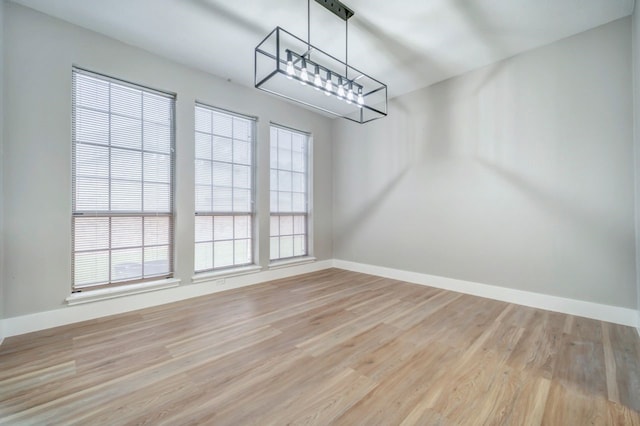 unfurnished dining area with baseboards, wood finished floors, and a chandelier