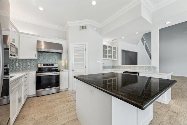 138 Isles End Rd, Tiki Island, TX 77554 - kitchen featuring stainless steel appliances, wall chimney exhaust hood, light wood-style flooring, white cabinets, and crown molding