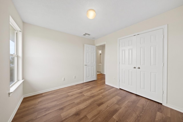 unfurnished bedroom featuring baseboards, multiple windows, wood finished floors, and visible vents