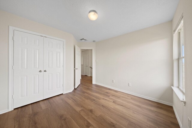 unfurnished bedroom with visible vents, baseboards, wood finished floors, and multiple windows