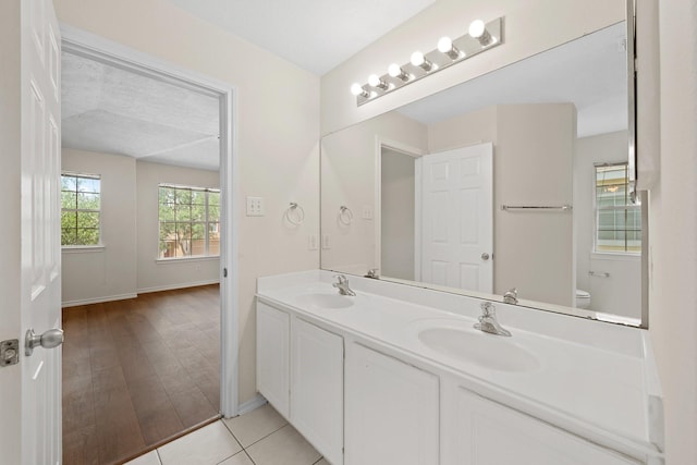 bathroom with baseboards, a sink, double vanity, and toilet