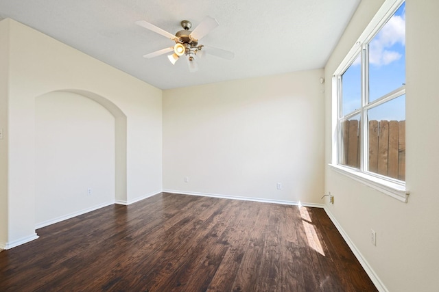 unfurnished room with arched walkways, a wealth of natural light, ceiling fan, and dark wood-type flooring