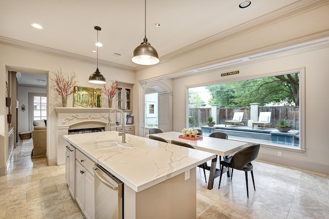kitchen featuring ornamental molding, a kitchen island with sink, a fireplace, light stone countertops, and a sink