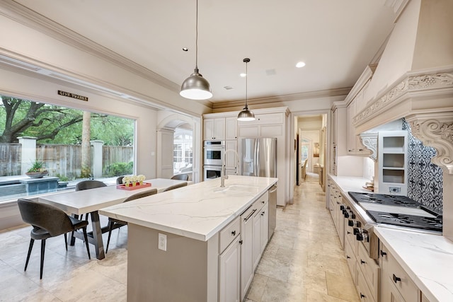 kitchen with crown molding, custom exhaust hood, an island with sink, appliances with stainless steel finishes, and hanging light fixtures
