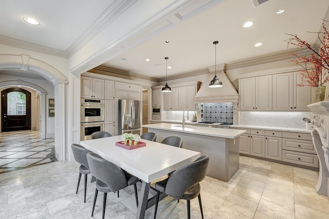 kitchen featuring a kitchen island with sink, premium range hood, light countertops, arched walkways, and appliances with stainless steel finishes