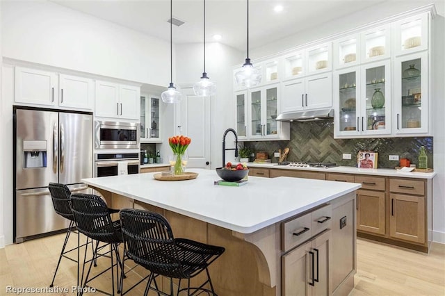 16427 Cat Ct, Conroe, TX 77302 - kitchen with decorative backsplash, a kitchen island with sink, appliances with stainless steel finishes, light countertops, and white cabinetry