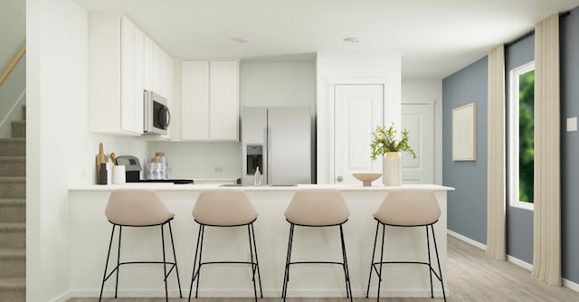 kitchen with a breakfast bar area, stainless steel microwave, fridge with ice dispenser, and white cabinets