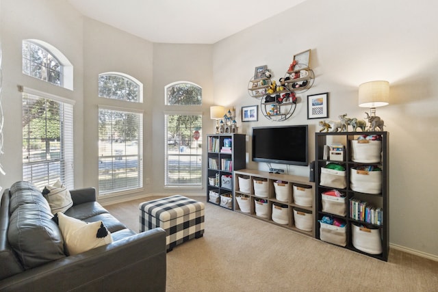 carpeted living room featuring baseboards, a towering ceiling, and a healthy amount of sunlight
