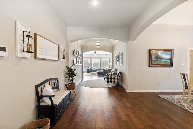 hall featuring baseboards, arched walkways, and wood finished floors
