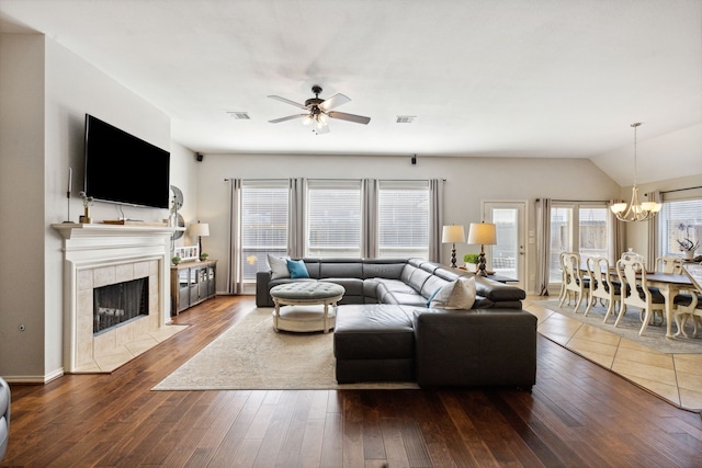 living area featuring a tiled fireplace, ceiling fan with notable chandelier, hardwood / wood-style floors, and visible vents