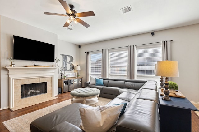 living area featuring a ceiling fan, visible vents, a tiled fireplace, and wood finished floors