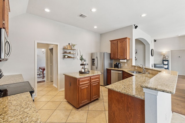 kitchen featuring arched walkways, a sink, light stone counters, a peninsula, and stainless steel appliances