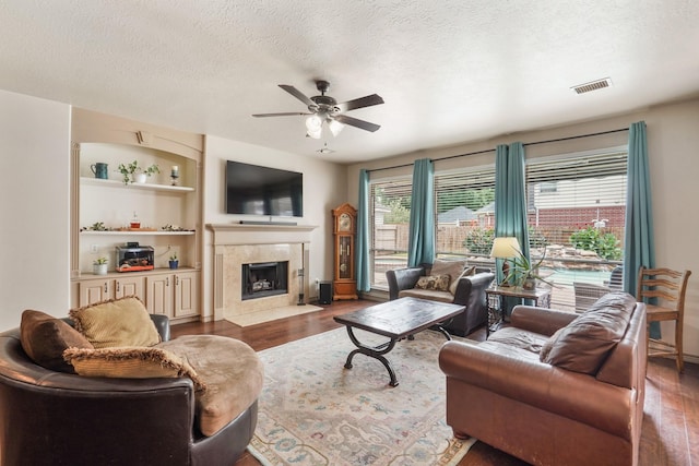 living room with built in features, wood finished floors, ceiling fan, a high end fireplace, and a textured ceiling