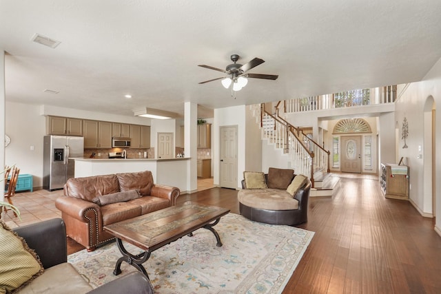 living area with arched walkways, a ceiling fan, baseboards, visible vents, and stairway