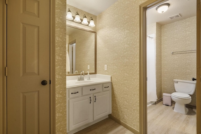 full bath with vanity, toilet, wallpapered walls, wood finished floors, and visible vents