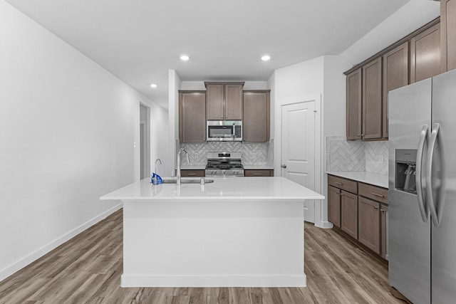 kitchen with backsplash, stainless steel appliances, a center island with sink, and a sink