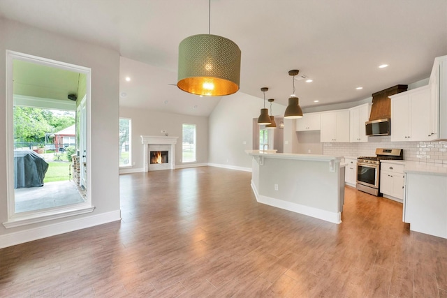 kitchen with appliances with stainless steel finishes, hanging light fixtures, light wood-type flooring, white cabinets, and open floor plan