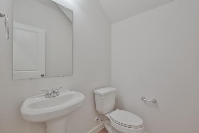 half bathroom with toilet, baseboards, vaulted ceiling, and a sink