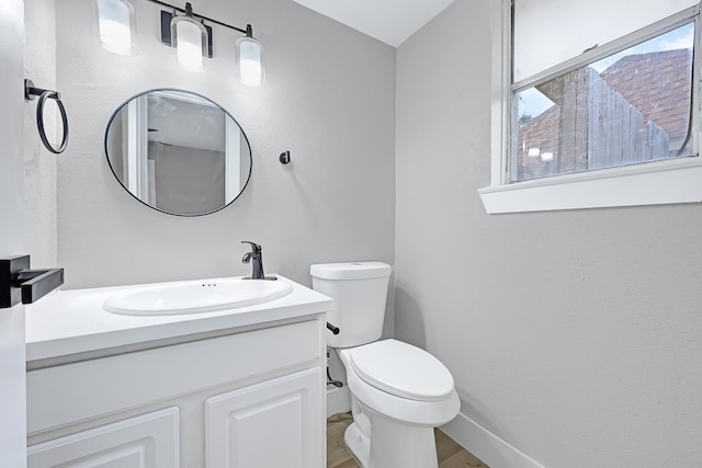 half bath featuring vanity, baseboards, wood finished floors, and toilet