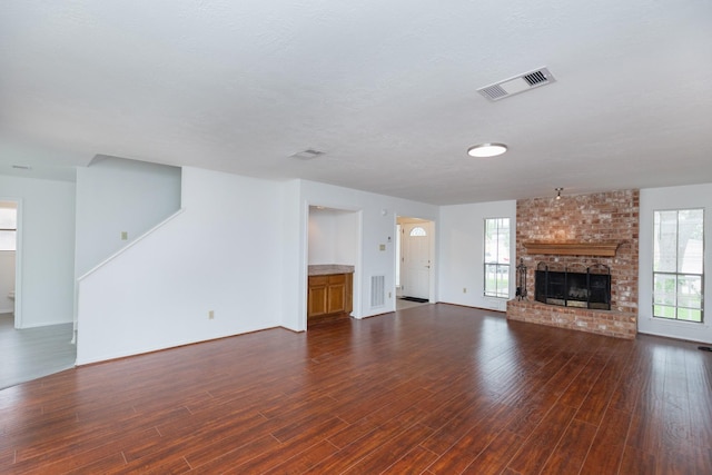 unfurnished living room with baseboards, visible vents, dark wood-style floors, and a fireplace