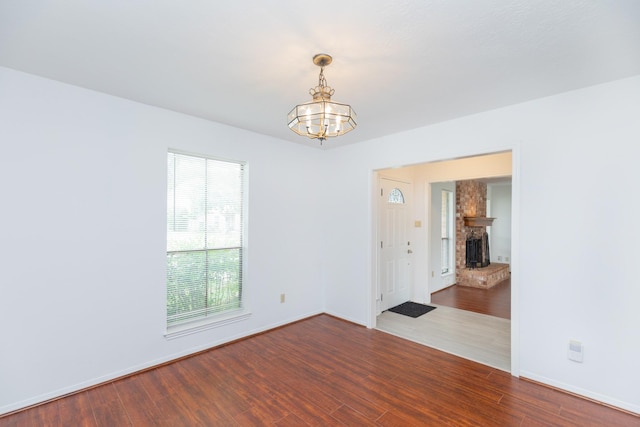 unfurnished room featuring a brick fireplace, baseboards, a notable chandelier, and wood finished floors