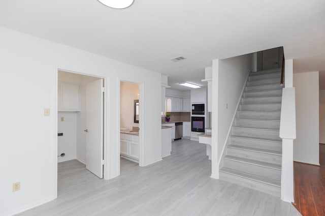 interior space featuring visible vents, light wood finished floors, baseboards, and stairway