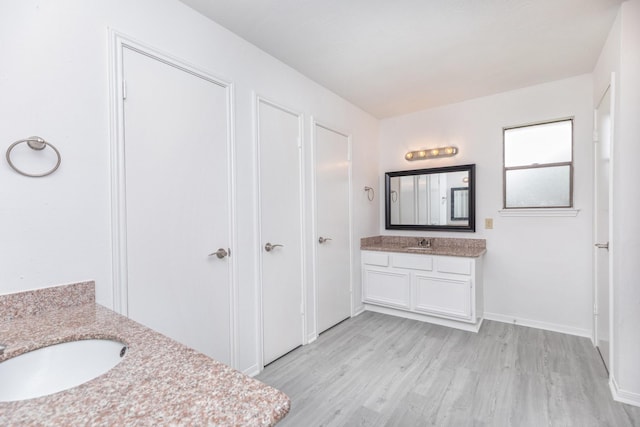bathroom with baseboards, a sink, two vanities, and wood finished floors