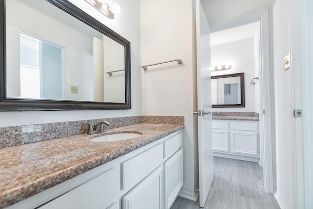 bathroom with wood finished floors, a sink, and two vanities