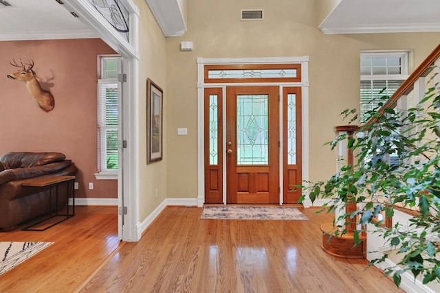 foyer with crown molding, baseboards, light wood-type flooring, and visible vents