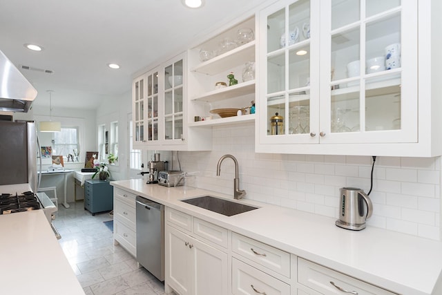 kitchen with white cabinets, appliances with stainless steel finishes, a sink, light countertops, and backsplash