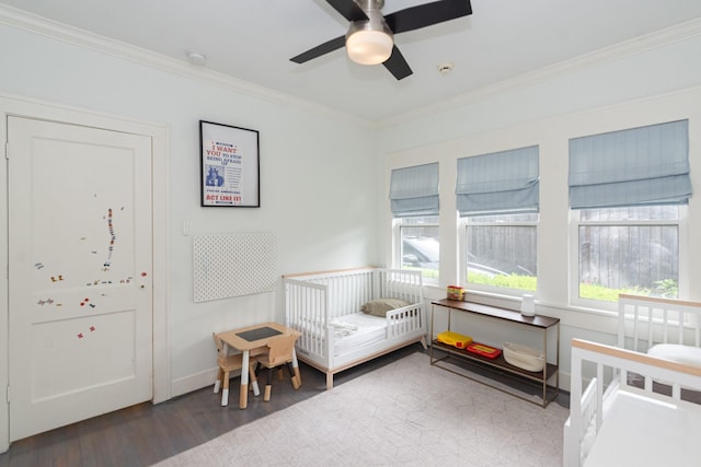 bedroom with crown molding, a nursery area, ceiling fan, and wood finished floors