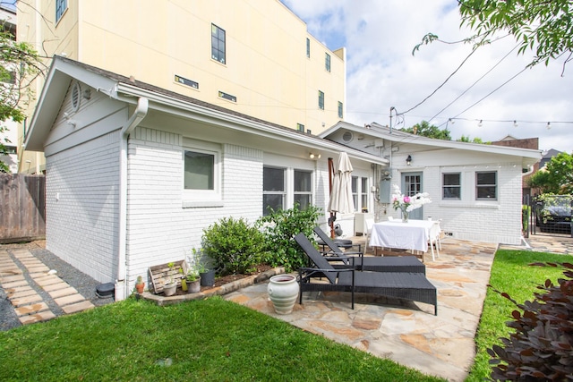 rear view of house featuring a lawn, brick siding, fence, and a patio