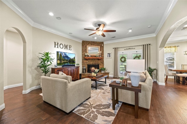 living area featuring a ceiling fan, a stone fireplace, crown molding, arched walkways, and wood finished floors