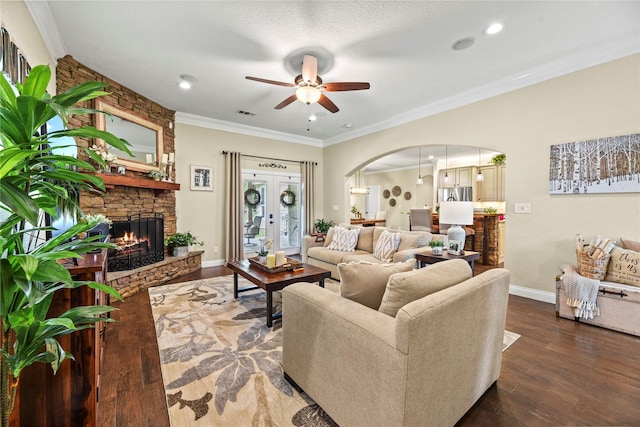 living room with arched walkways, a ceiling fan, a stone fireplace, and wood finished floors
